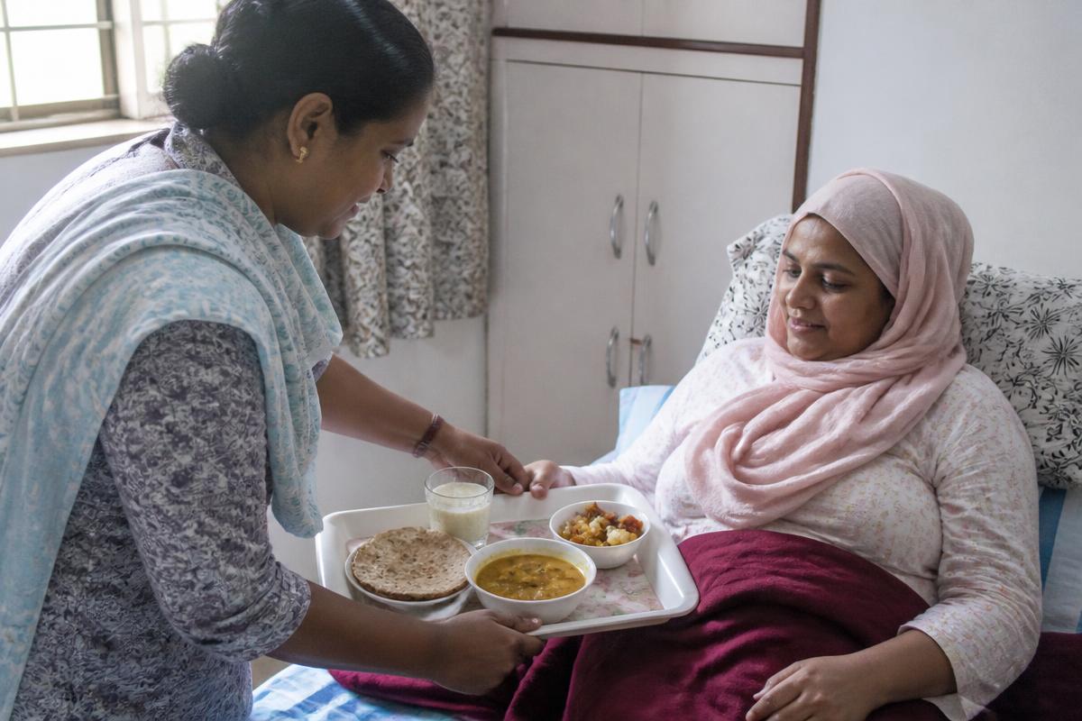 Caregiver serving a home-cooked meal to a cancer patient resting in bed