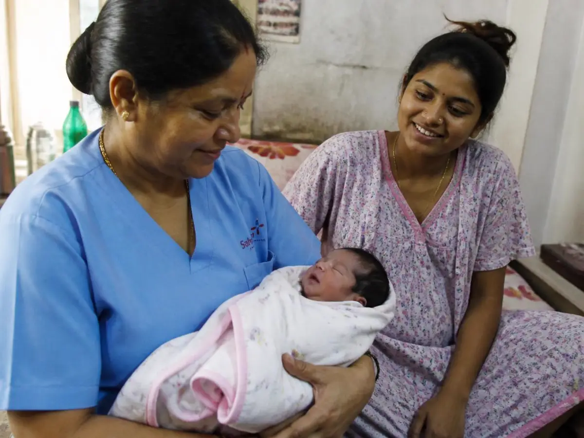 Home nurse swaddling a newborn baby beside the mother in Mumbai