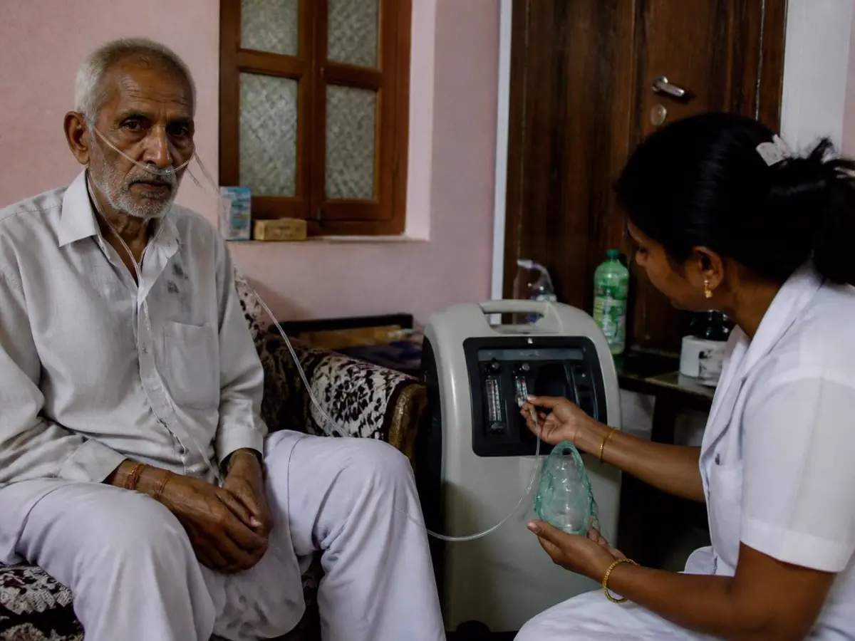Elderly patient on oxygen therapy at home while a nurse adjusts the concentrator